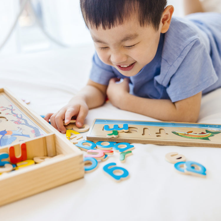 A kid playing with The Melissa & Doug See & Spell Wooden Educational Toy With 8 Double-Sided Spelling Boards and 64 Letters
