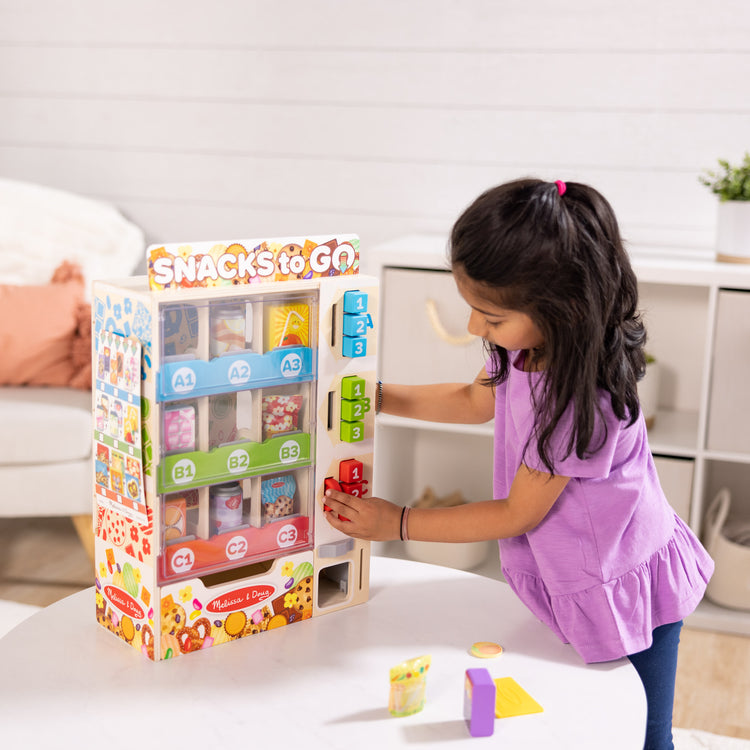 A kid playing with The Melissa & Doug Sort, Stock, Select Wooden Vending Machine Play Set, Wooden Toy Play Food For Boys and For Girls 3+