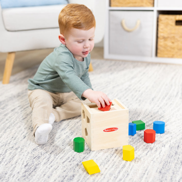 A kid playing with The Melissa & Doug Shape Sorting Cube - Classic Wooden Toy With 12 Shapes