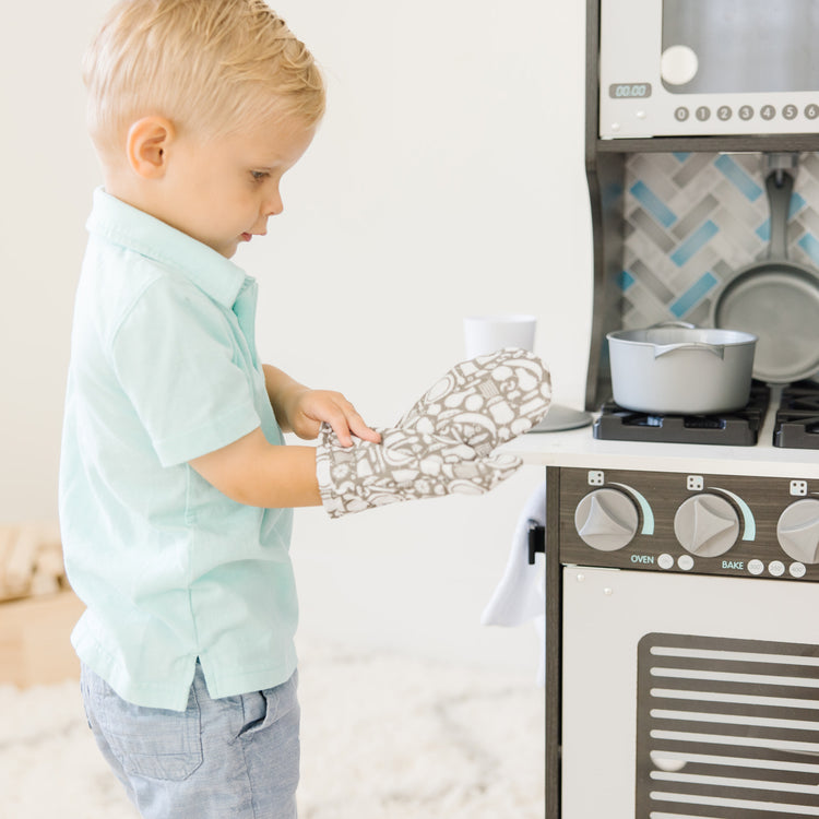 A kid playing with The Melissa & Doug Chef's Wooden Pretend Play Kitchen for Kids With “Ice” Cube Dispenser – Charcoal Gray