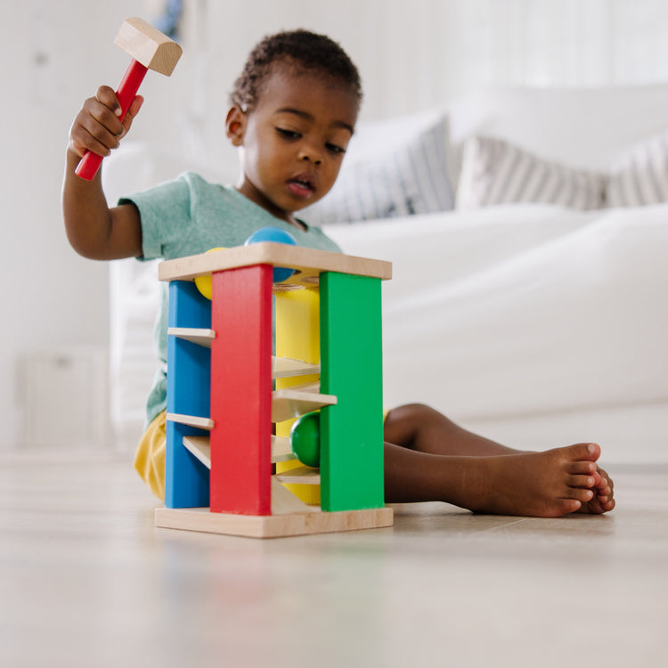 A kid playing with The Melissa & Doug Deluxe Pound and Roll Wooden Tower Toy With Hammer