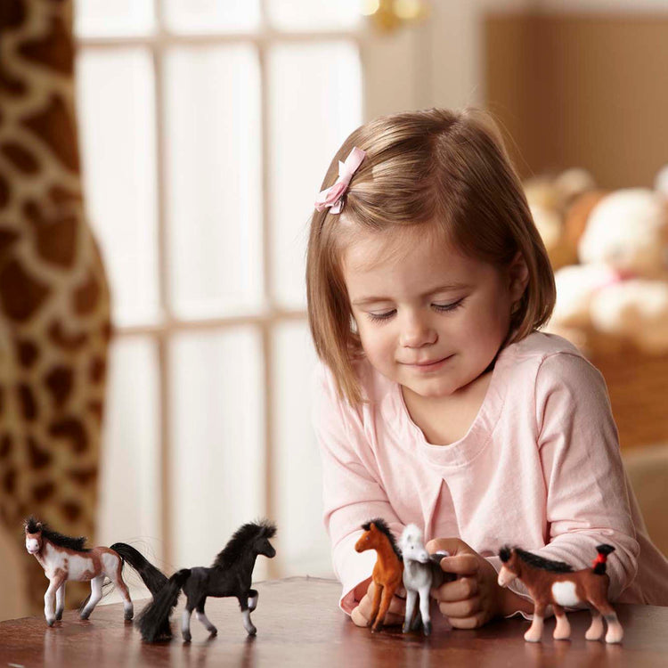 A child on white background with The Melissa & Doug Pasture Pals - 12 Collectible Horses With Wooden Barn-Shaped Crate