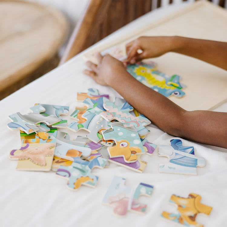 A kid playing with The Melissa & Doug Under the Sea Ocean Animals Wooden Jigsaw Puzzle With Storage Tray (24 pcs)