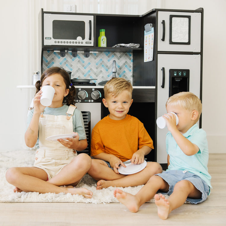 A kid playing with The Melissa & Doug Chef's Wooden Pretend Play Kitchen for Kids With “Ice” Cube Dispenser – Charcoal Gray