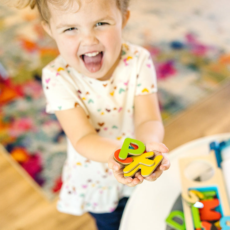 A kid playing with The Melissa & Doug 52 Wooden Alphabet Magnets in a Box - Uppercase and Lowercase Letters