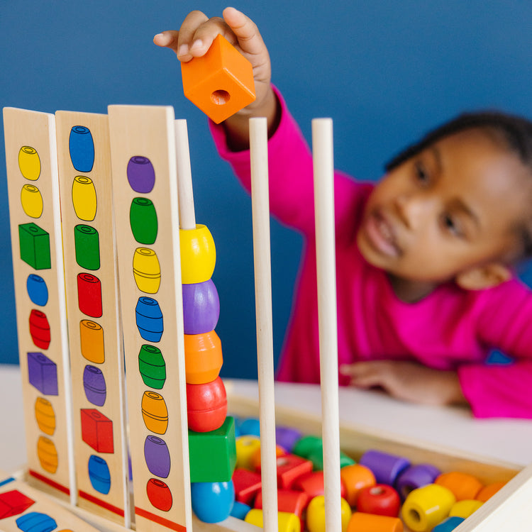 A kid playing with The Melissa & Doug Bead Sequencing Set With 46 Wooden Beads and 5 Double-Sided Pattern Boards