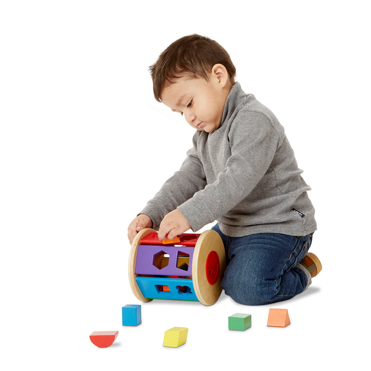 A child on white background with The Melissa & Doug Match and Roll Shape Sorter - Classic Wooden Toy