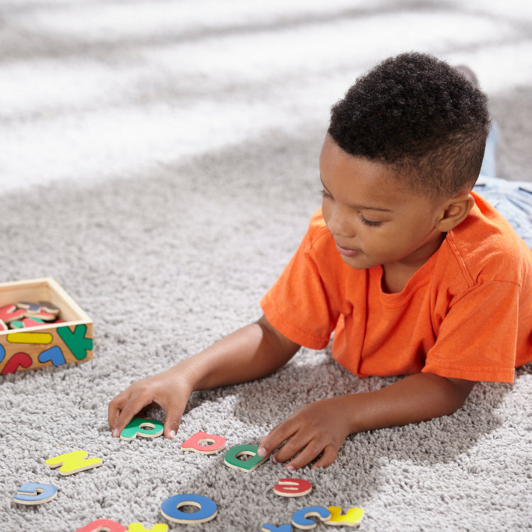 A kid playing with The Melissa & Doug 52 Wooden Alphabet Magnets in a Box - Uppercase and Lowercase Letters