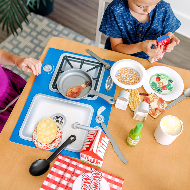 A kid playing with The Melissa & Doug Deluxe Kitchen Collection Cooking & Play Food Set – 58 Pieces