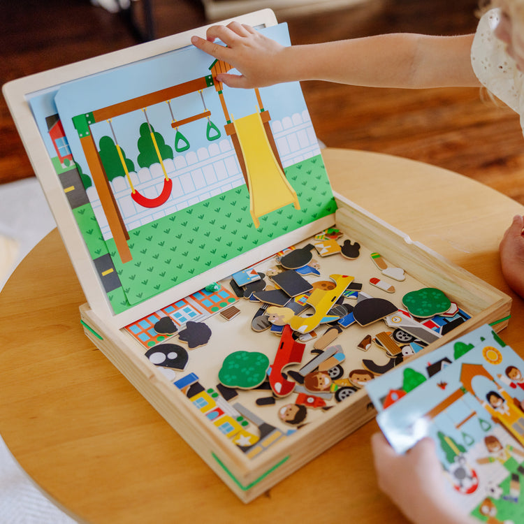 A kid playing with The Melissa & Doug Wooden Magnetic Matching Picture Game With 119 Magnets and Scene Cards