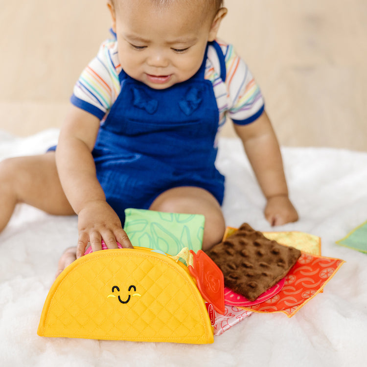 A kid playing with The Melissa & Doug Multi-Sensory Soft Taco Fill & Spill Infant Toy