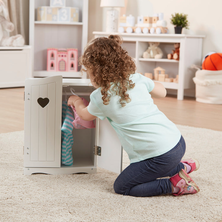 A kid playing with The Melissa & Doug Mine to Love Wooden Play Armoire Closet for Dolls, Stuffed Animals - White (17.3”H x 12.4”W x 8.5”D Assembled)