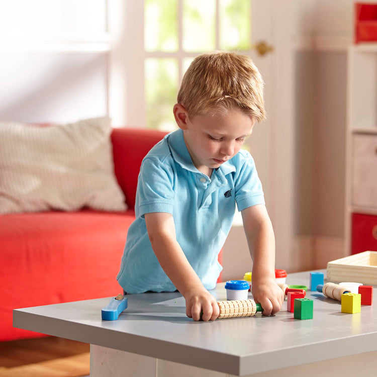 A kid playing with The Melissa & Doug Shape, Model, and Mold Craft Activity Set - 4 Tubs of Modeling Dough and Tools