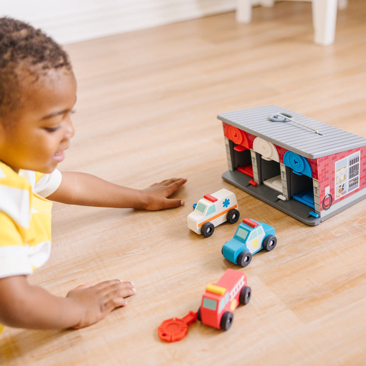 A kid playing with The Melissa & Doug Toy Keys and Cars Wooden Rescue Vehicles and Garage (7 pcs)