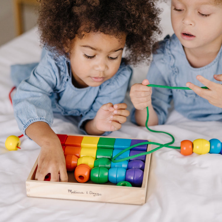 A kid playing with The Melissa & Doug Primary Lacing Beads - Educational Toy With 30 Wooden Beads and 2 Laces