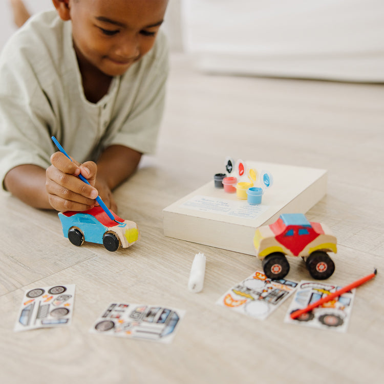 A kid playing with The Melissa & Doug Decorate-Your-Own Wooden Craft Kits Set - Race Car and Monster Truck