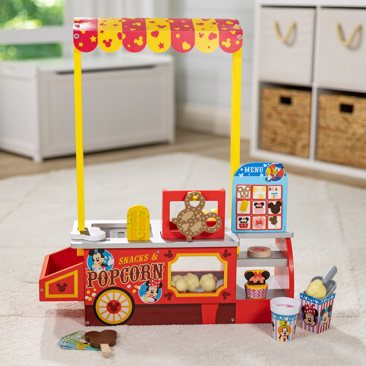 A playroom scene with The Melissa & Doug Disney Snacks & Popcorn Wooden Pretend Play Food Counter – 33 Pieces