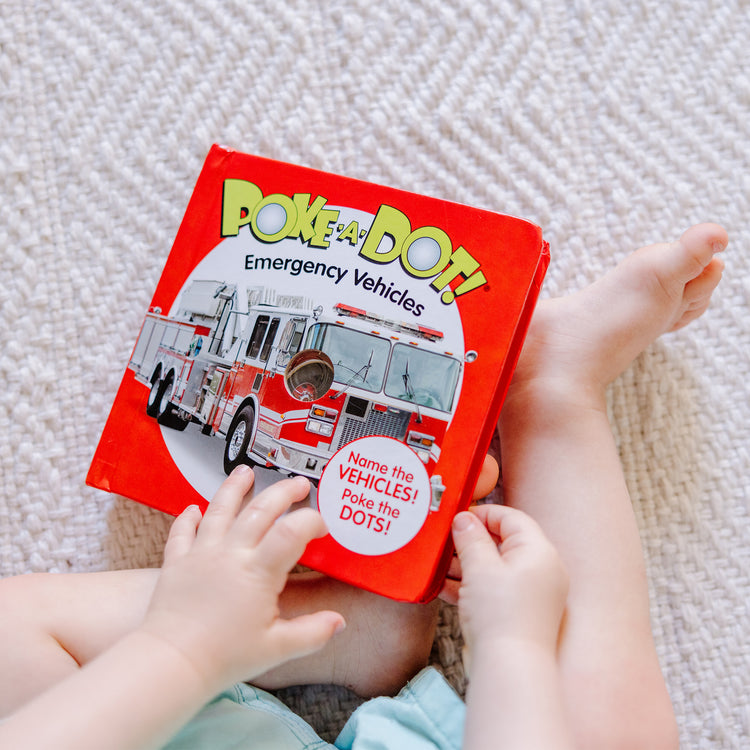 A kid playing with The Melissa & Doug Children’s Book – Poke-a-Dot: Emergency Vehicles (Board Book with Buttons to Pop)