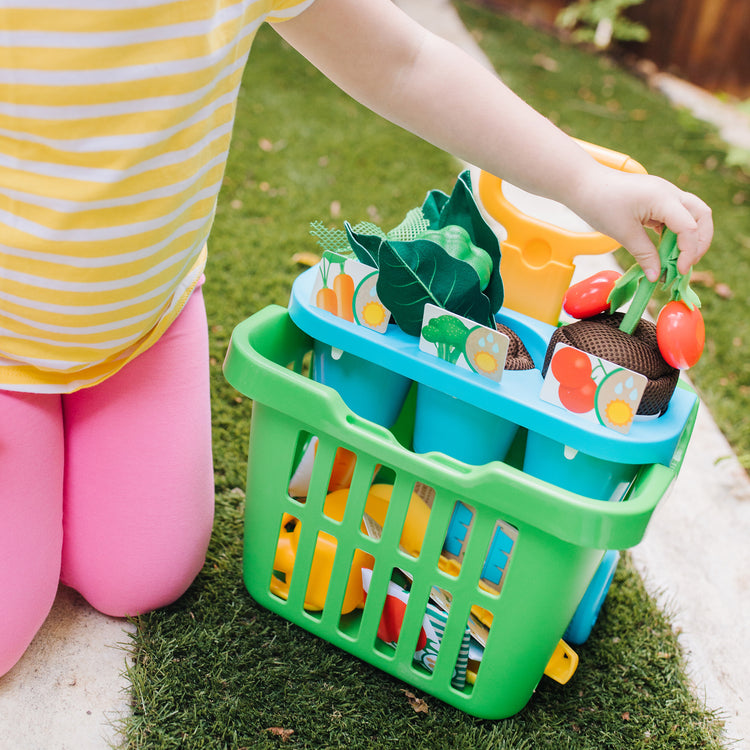 A kid playing with The Melissa & Doug Let’s Explore Vegetable Gardening Play Set with Rolling Cart (31 Pieces)