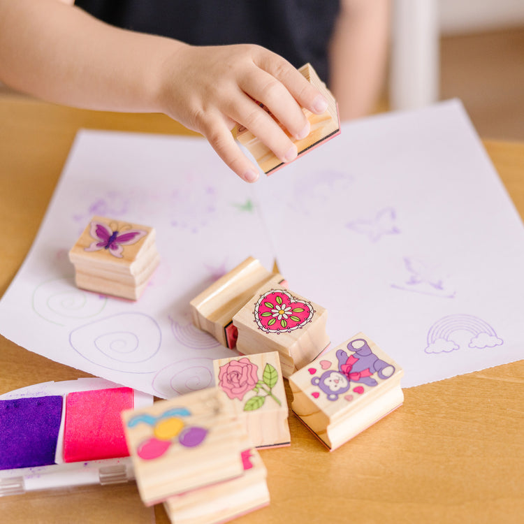 A kid playing with The Melissa & Doug Wooden Stamp Set: Friendship - 9 Stamps, 5 Colored Pencils, and 2-Color Stamp Pad