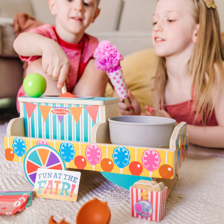 A kid playing with The Melissa & Doug Fun at the Fair! Wooden Carnival Candy Tabletop Cart and Play Food Set