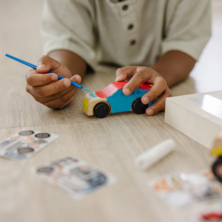 A kid playing with The Melissa & Doug Decorate-Your-Own Wooden Craft Kits Set - Race Car and Monster Truck