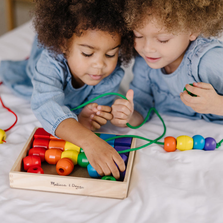 A kid playing with The Melissa & Doug Primary Lacing Beads - Educational Toy With 30 Wooden Beads and 2 Laces