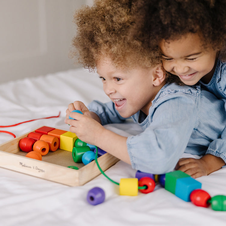 A kid playing with The Melissa & Doug Primary Lacing Beads - Educational Toy With 30 Wooden Beads and 2 Laces