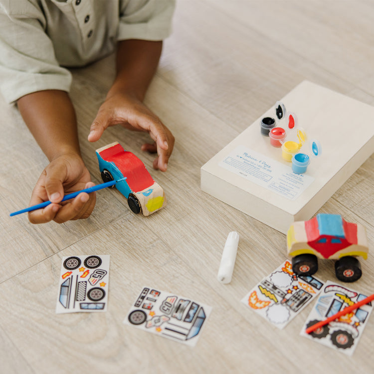 A kid playing with The Melissa & Doug Decorate-Your-Own Wooden Craft Kits Set - Race Car and Monster Truck