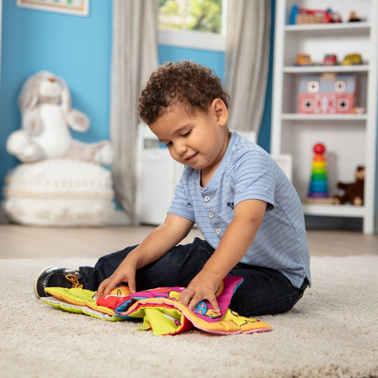 A kid playing with The Melissa & Doug K’s Kids Whose Bone? 8-Page Soft Activity Book for Babies and Toddlers