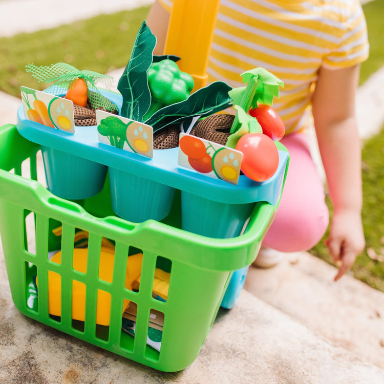 A kid playing with The Melissa & Doug Let’s Explore Vegetable Gardening Play Set with Rolling Cart (31 Pieces)