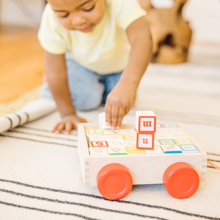 A kid playing with The Melissa & Doug Classic ABC Wooden Block Cart Educational Toy With 30 1-Inch Solid Wood Blocks