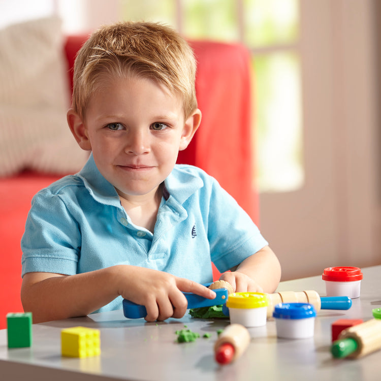 A kid playing with The Melissa & Doug Shape, Model, and Mold Craft Activity Set - 4 Tubs of Modeling Dough and Tools