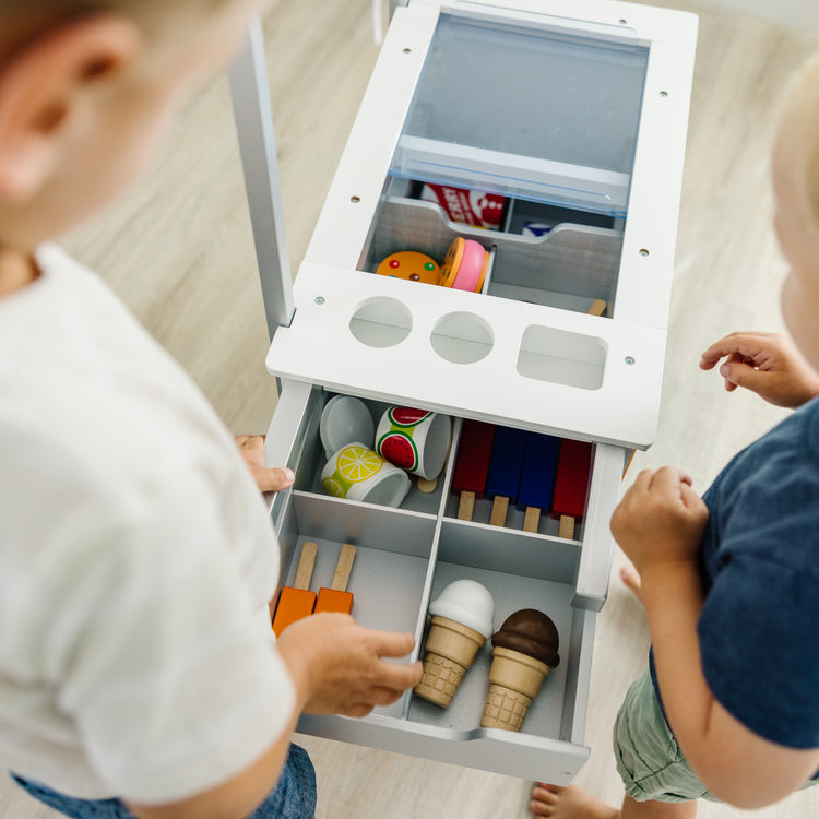 A kid playing with The Melissa & Doug Wooden Snacks and Sweets Food Cart - 40+ Play Food pcs, Reversible Awning