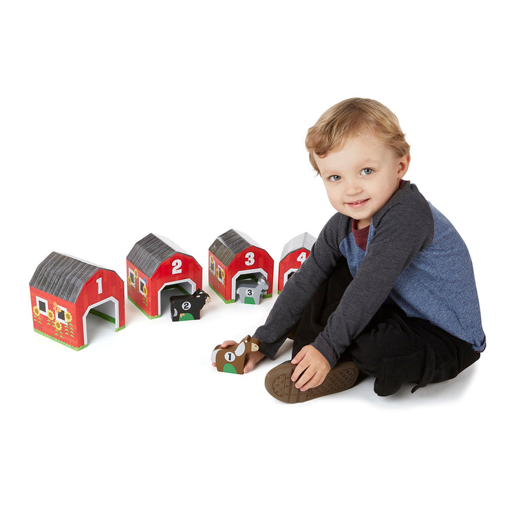 A child on white background with The Melissa & Doug Nesting and Sorting Barns and Animals With 6 Numbered Barns and Matching Wooden Animals