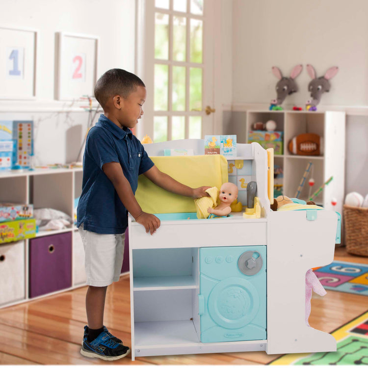 A kid playing with The Melissa & Doug Mine to Love Baby Care Activity Center for Dolls - Kitchen, Nursery, Bathing-Changing