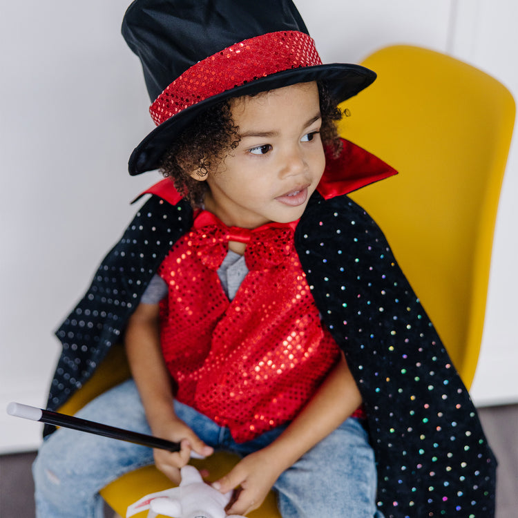 A kid playing with The Melissa & Doug Magician Costume Role Play Set - Includes Hat, Cape, Wand, Magic Tricks