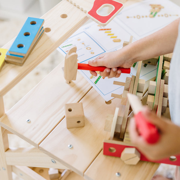 A kid playing with The Melissa & Doug Solid Wood Project Workbench Play Building Set