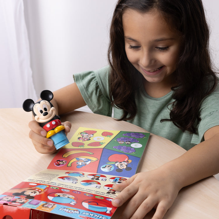 A kid playing with The Melissa & Doug Sticker WOW!™ 24-Page Activity Pad and Sticker Stamper, 300 Stickers, Arts and Crafts Fidget Toy Collectible Character – Disney Mickey Mouse

