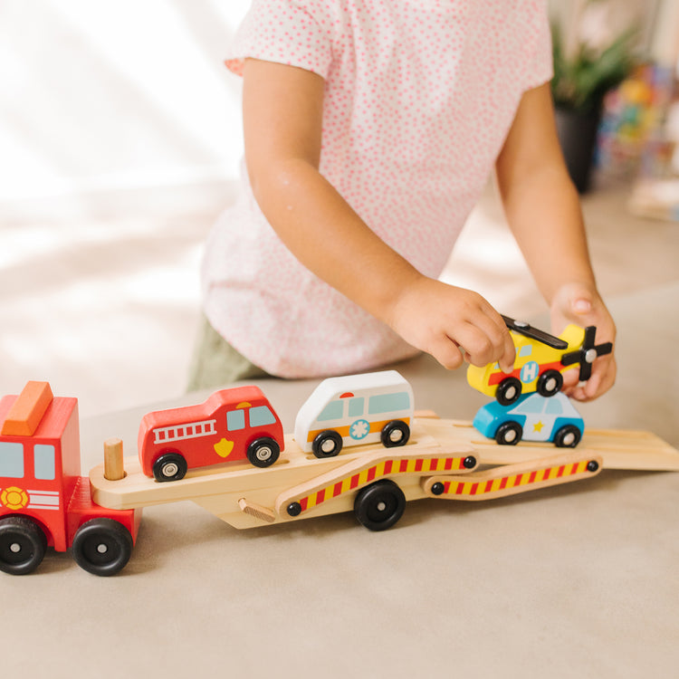 A kid playing with The Melissa & Doug Emergency Vehicle Carrier Wooden Truck With 4 Rescue Vehicles