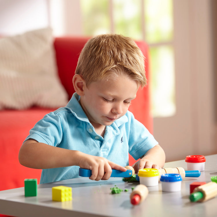 A kid playing with The Melissa & Doug Shape, Model, and Mold Craft Activity Set - 4 Tubs of Modeling Dough and Tools