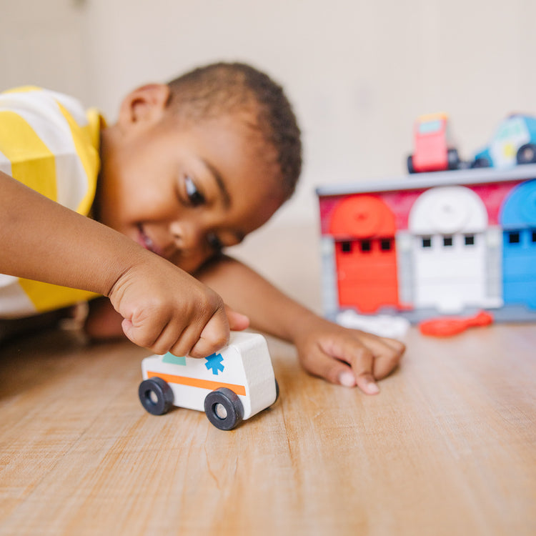 A kid playing with The Melissa & Doug Toy Keys and Cars Wooden Rescue Vehicles and Garage (7 pcs)