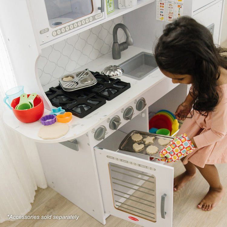 A kid playing with The Melissa & Doug Wooden Chef’s Pretend Play Toy Kitchen With “Ice” Cube Dispenser – Cloud White