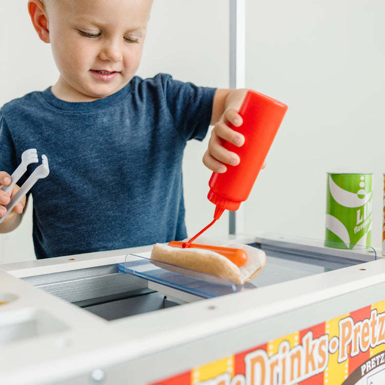 A kid playing with The Melissa & Doug Wooden Snacks and Sweets Food Cart - 40+ Play Food pcs, Reversible Awning