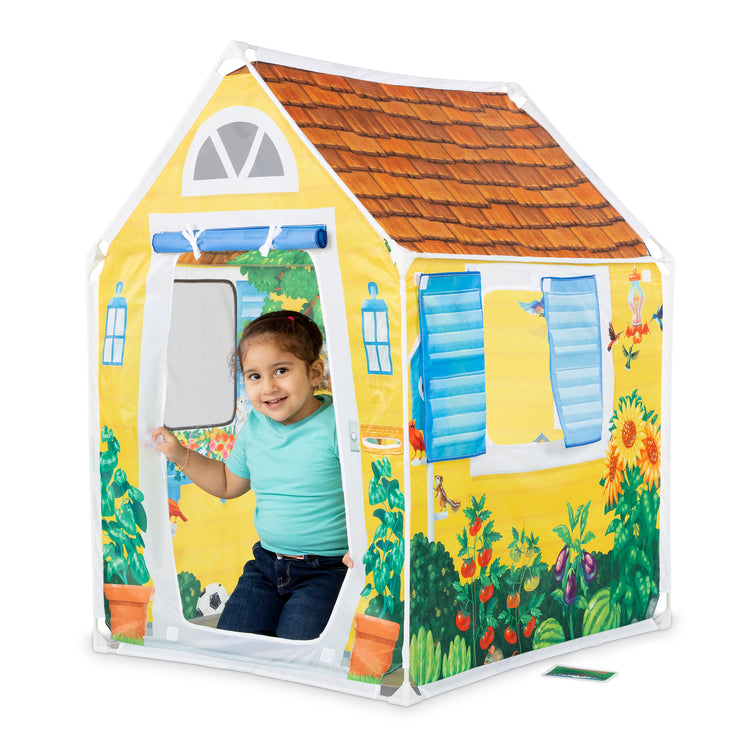 A child on white background with The Melissa & Doug Cozy Cottage Fabric Play Tent and Storage Tote