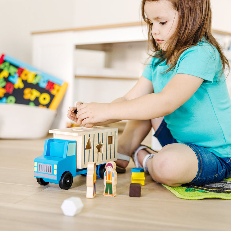 A kid playing with The Melissa & Doug Shape-Sorting Wooden Dump Truck Toy With 9 Colorful Shapes and 2 Play Figures