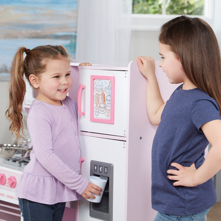 A kid playing with The Melissa & Doug Wooden Chef’s Pretend Play Toy Kitchen With “Ice” Cube Dispenser – Cupcake Pink/White