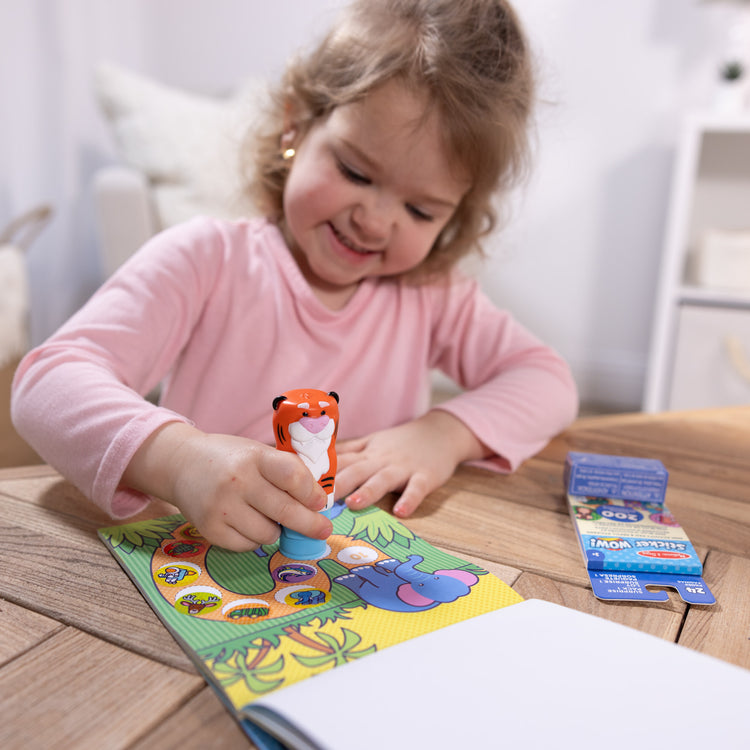 A kid playing with The Melissa & Doug Sticker WOW!™ Tiger Bundle: 24-Page Activity Pad, Sticker Stamper, 500 Stickers, Arts and Crafts Fidget Toy Collectible Character