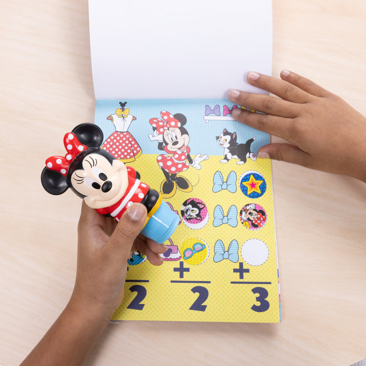 A kid playing with The Melissa & Doug Sticker WOW!™ 24-Page Activity Pad and Sticker Stamper, 300 Stickers, Arts and Crafts Fidget Toy Collectible Character – Disney Minnie Mouse