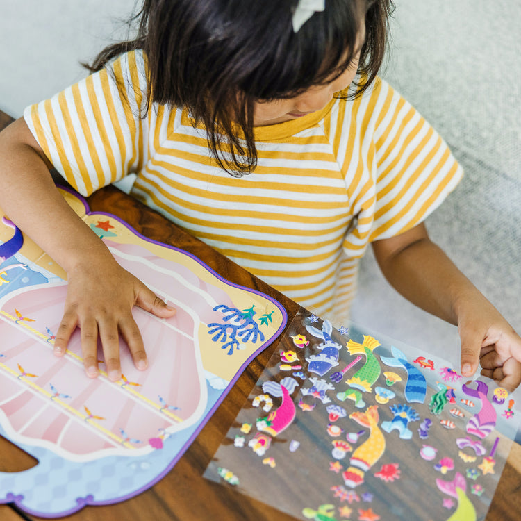 A kid playing with The Melissa & Doug Puffy Sticker Activity Book: Mermaids - 65 Reusable Stickers